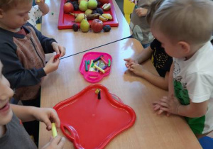 Dzieci stoją przy stoliku i z plasteliny robią owoce